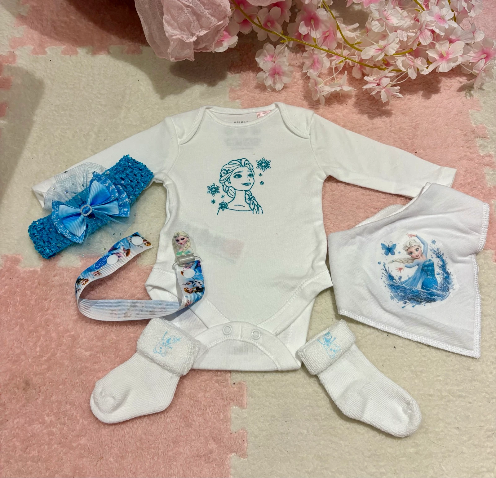 Ensemble bébé – Body + bavoir + attache tétine + bandeau + chaussettes